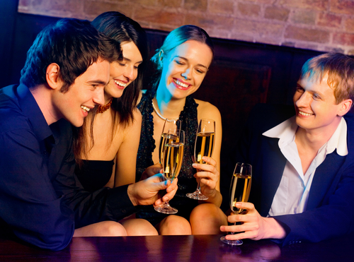 Two happy smiling young couples with champagne at celebration, party or romantic date at club